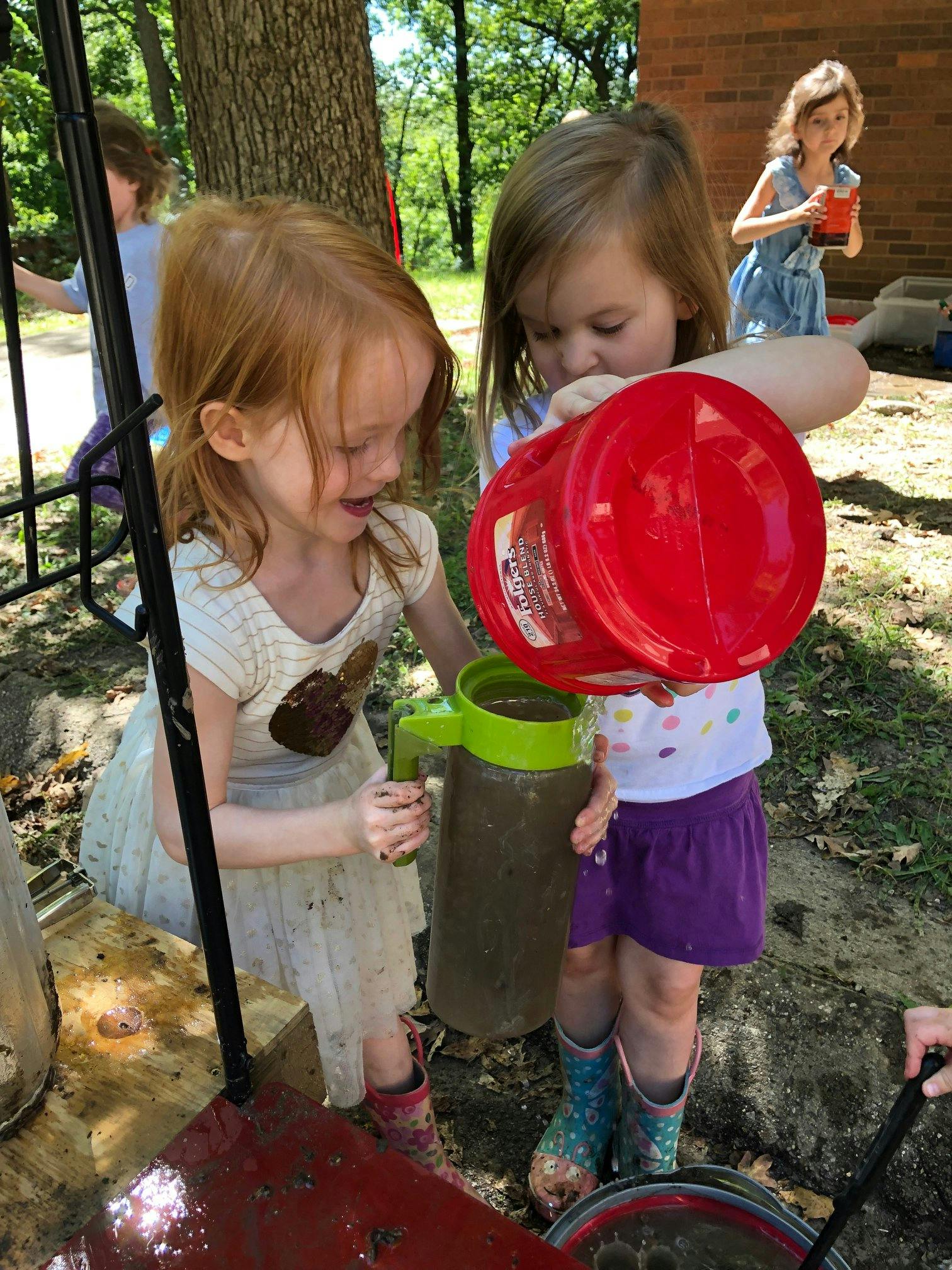 Two children pouring liquid from a red container into a pitcher