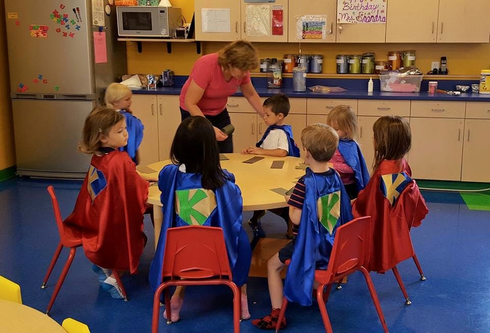 Adult with children in superhero capes sitting around a table