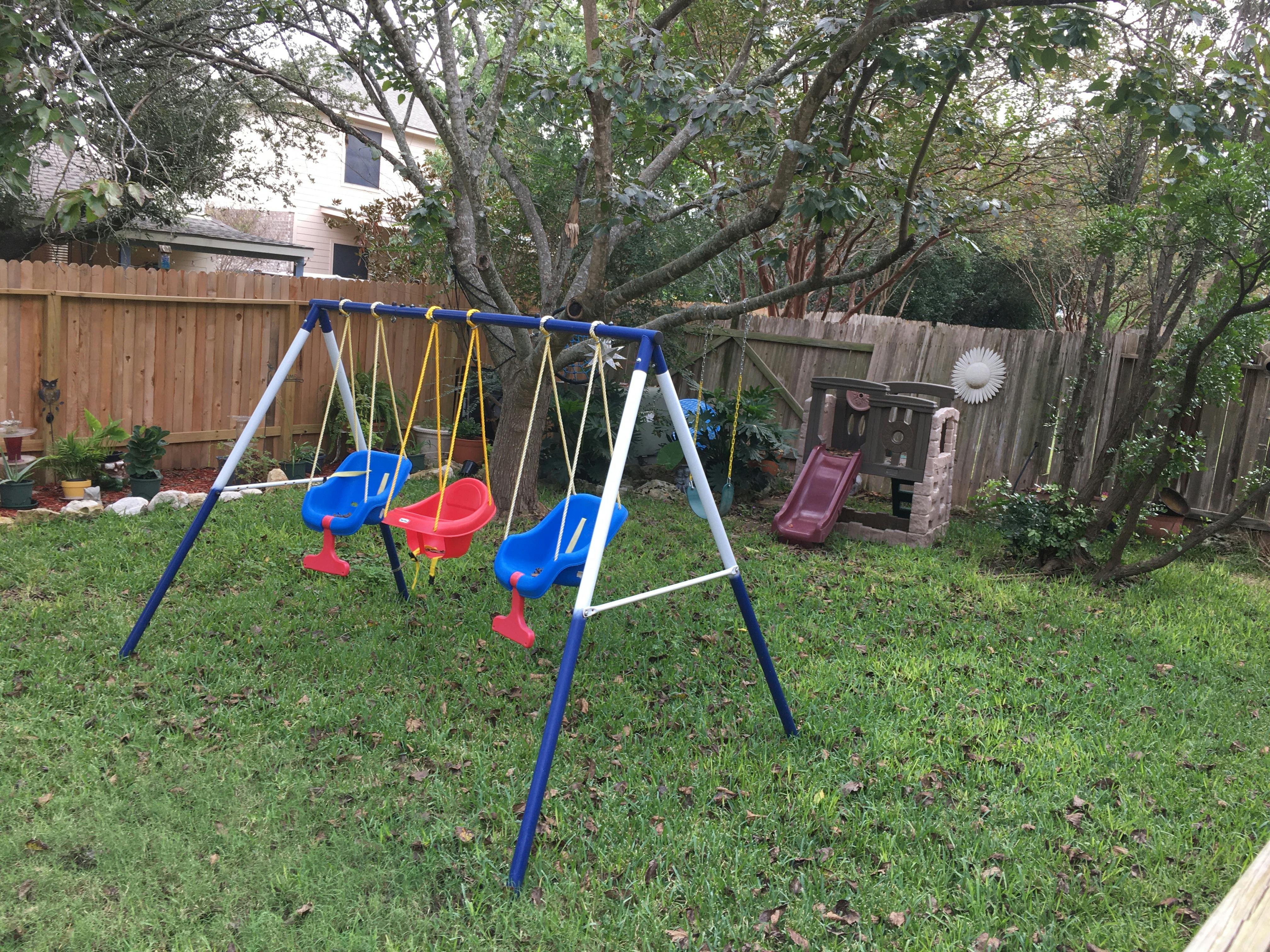 Swing set with three swings and a small slide in a grassy yard