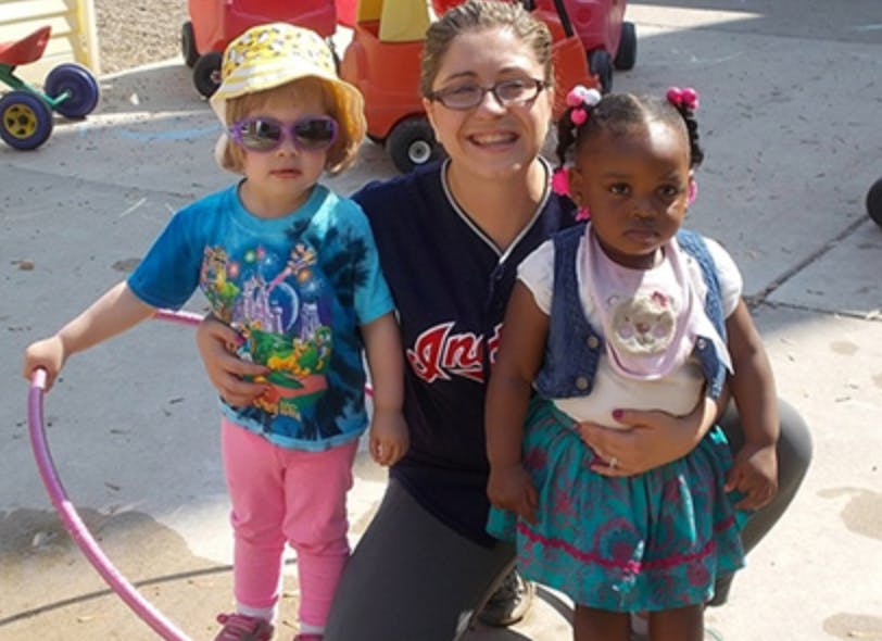 Person kneeling with two children, one holding a hula hoop