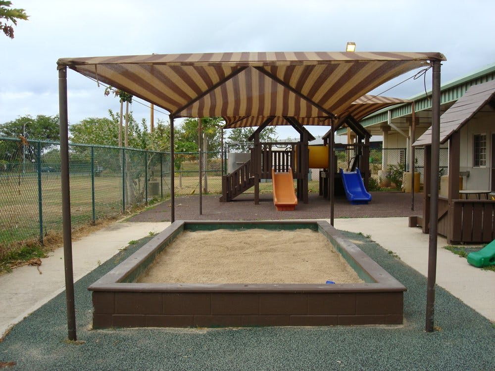 Sandbox with a striped canopy and a playground in the background