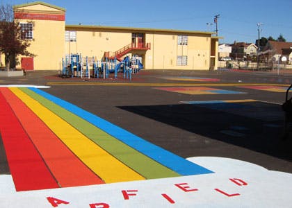 Rainbow painted on a school playground with a building and play structure