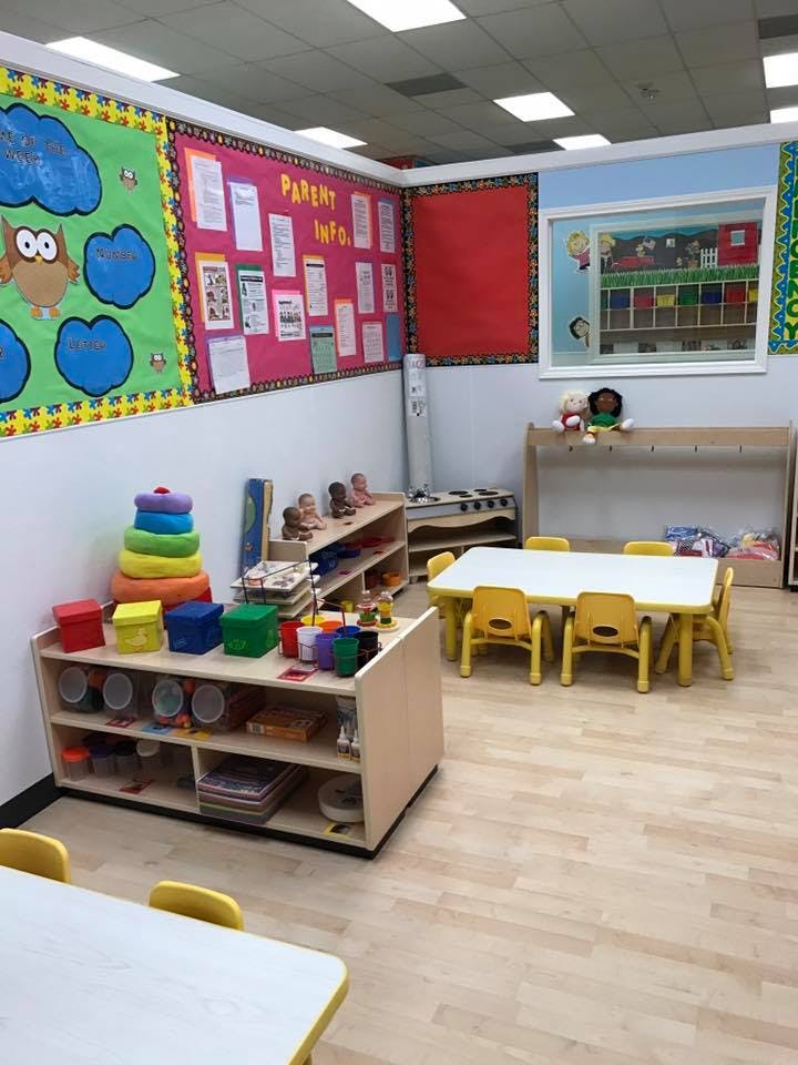 Classroom with small tables and chairs, shelves with toys, and bulletin boards