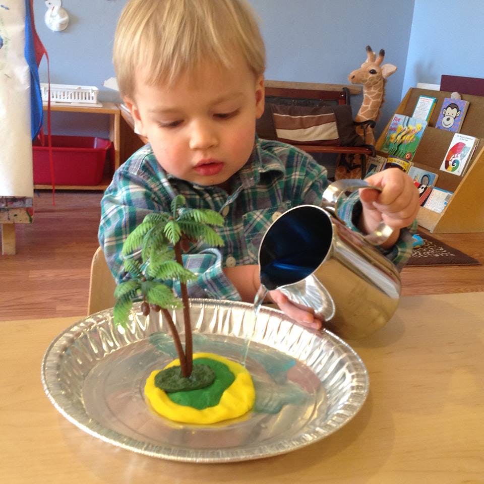 Child pouring water from a pitcher onto a small island with a palm tree