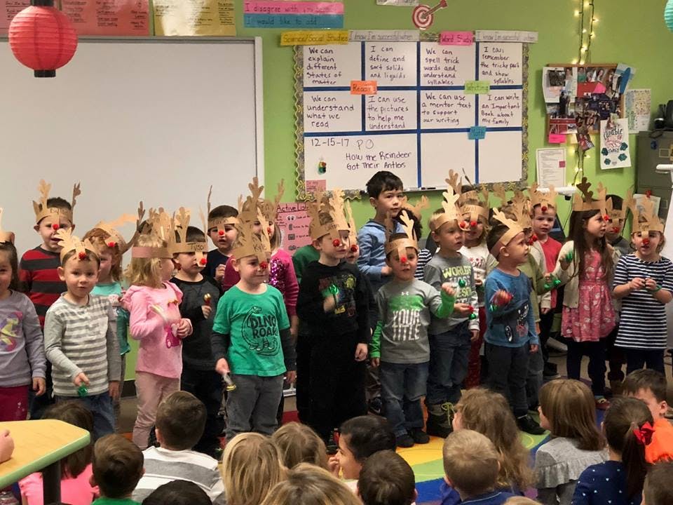 Children wearing reindeer antlers and red noses in a classroom