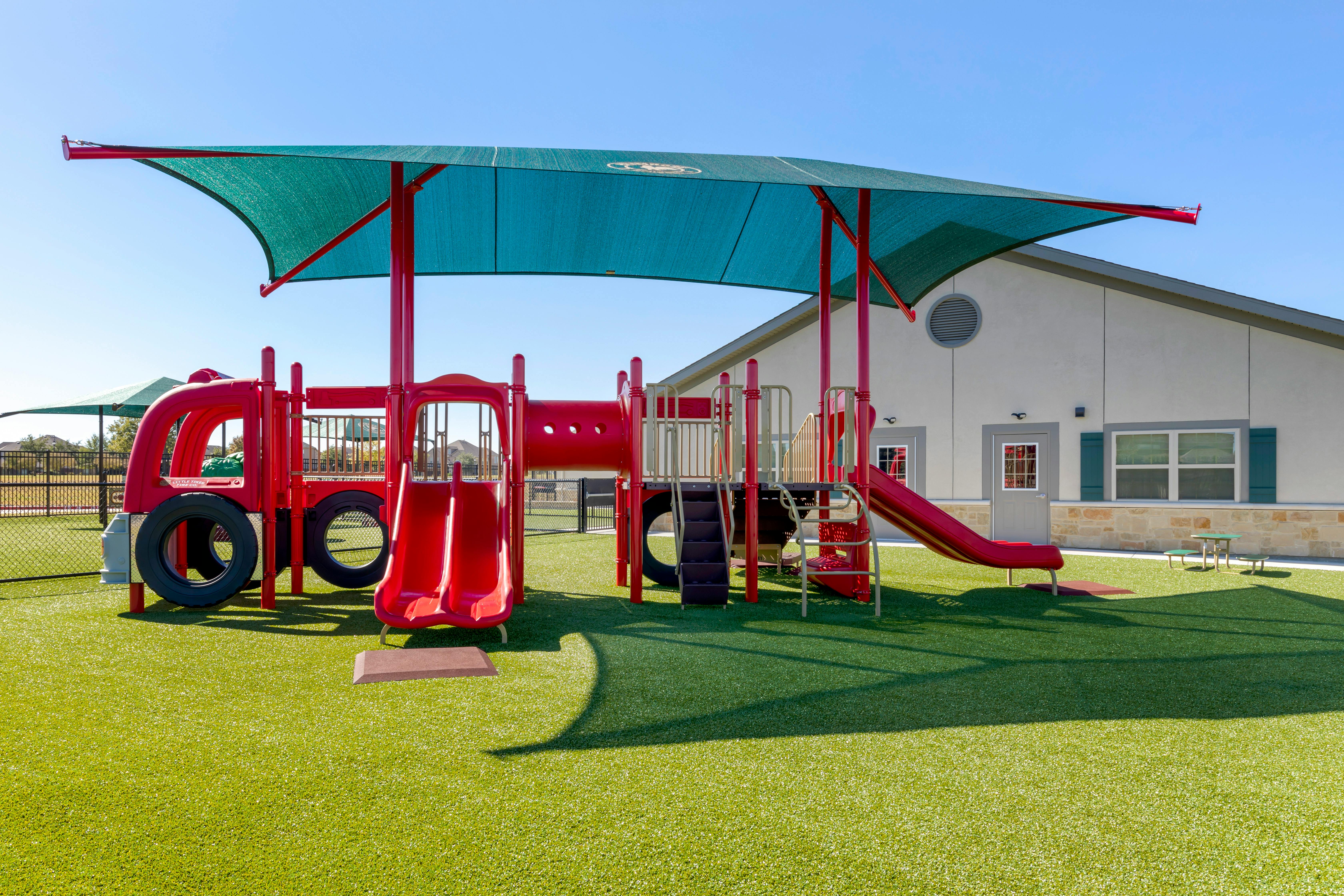 Red playground structure with slides and a tunnel on artificial green grass
