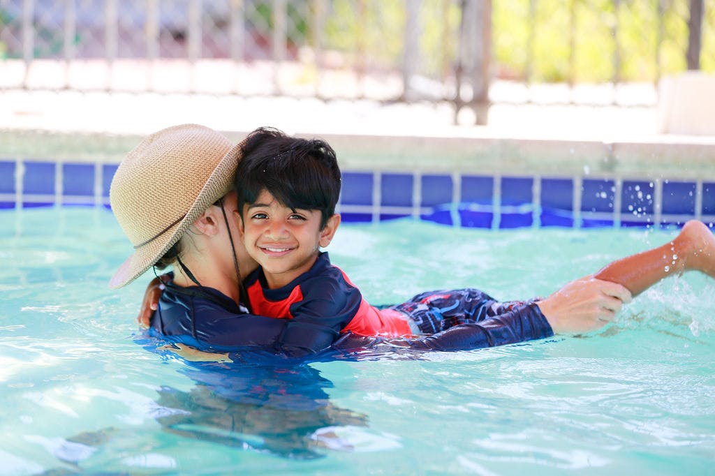 Person in a hat holding a child in a swimming pool