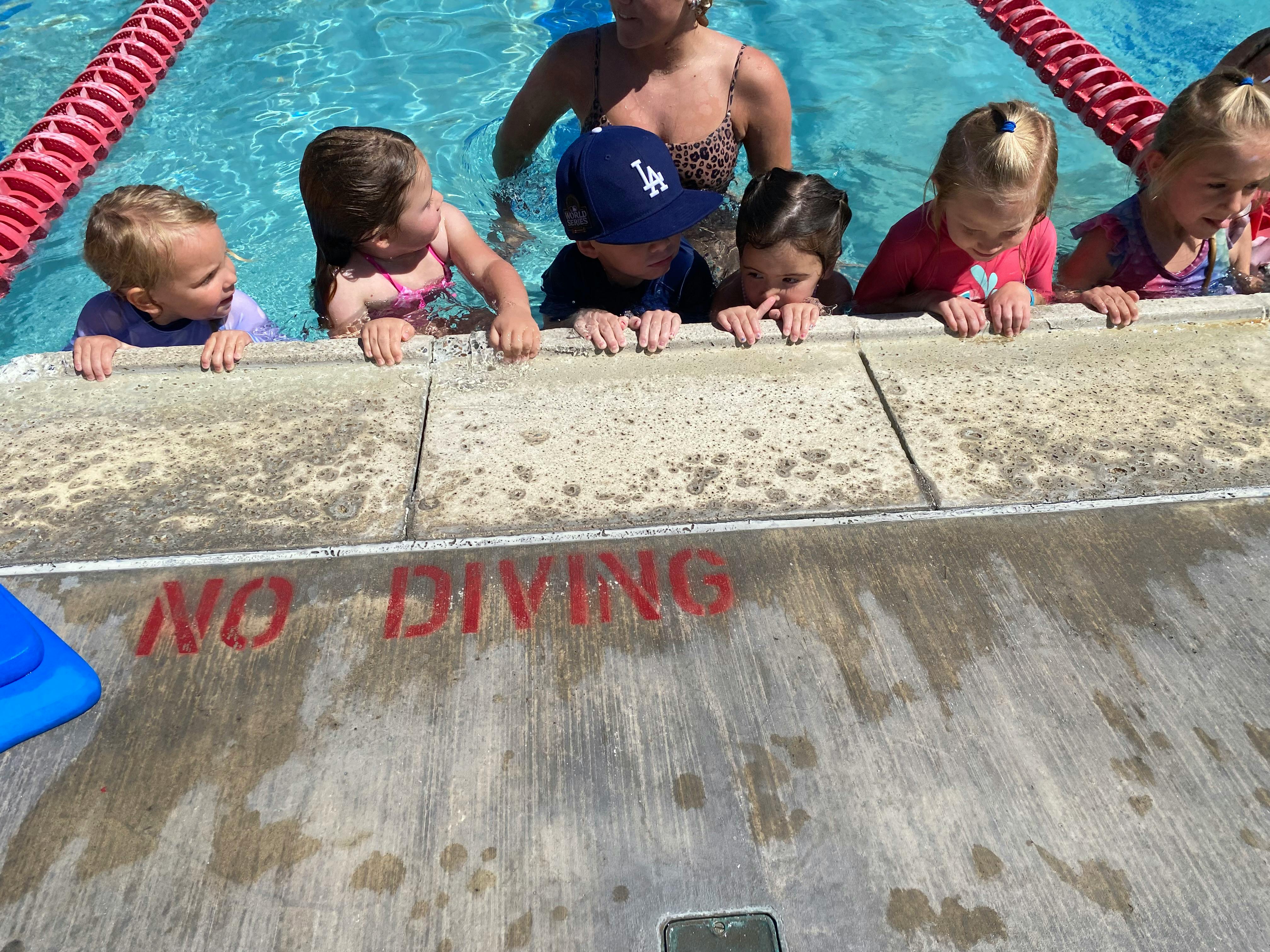 Children in a pool looking over the edge with "NO DIVING" painted on the deck