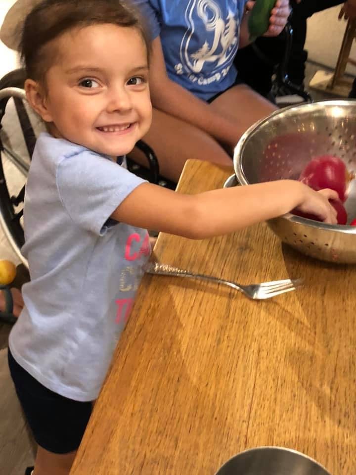 Child reaching into a bowl of red fruit on a wooden table