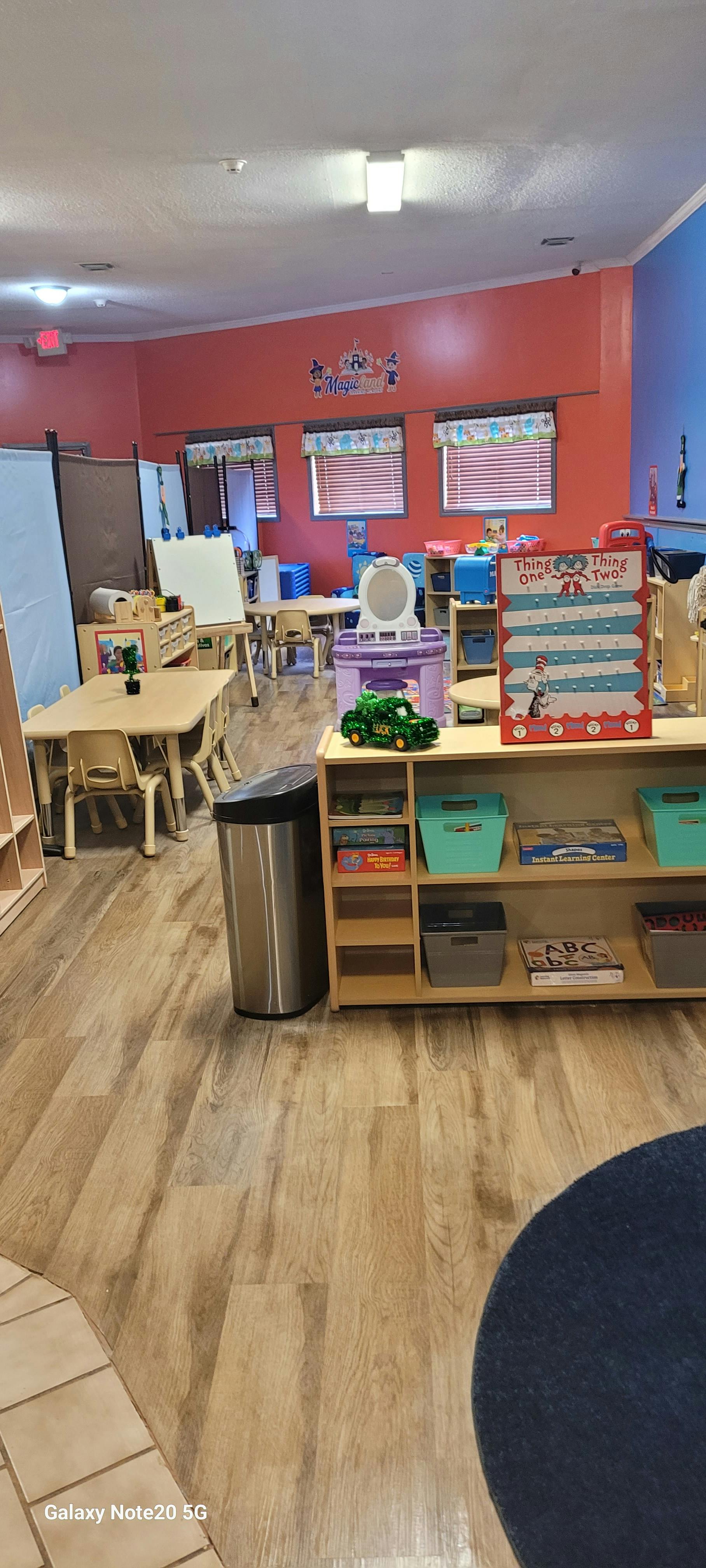 Classroom with small tables and chairs, shelves with toys, and a trash can
