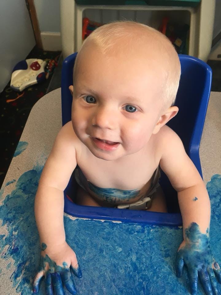 Child in high chair with blue paint on hands and tray