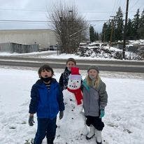 Three children standing next to a snowman