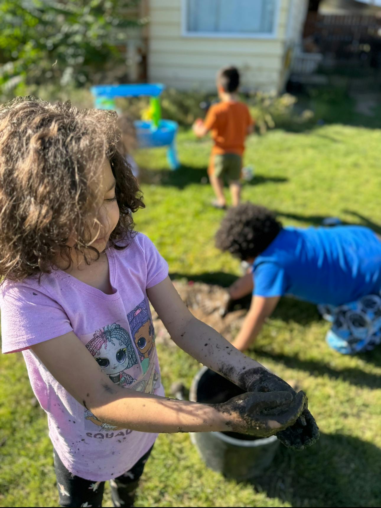 Child with muddy hands holding mud over a bucket