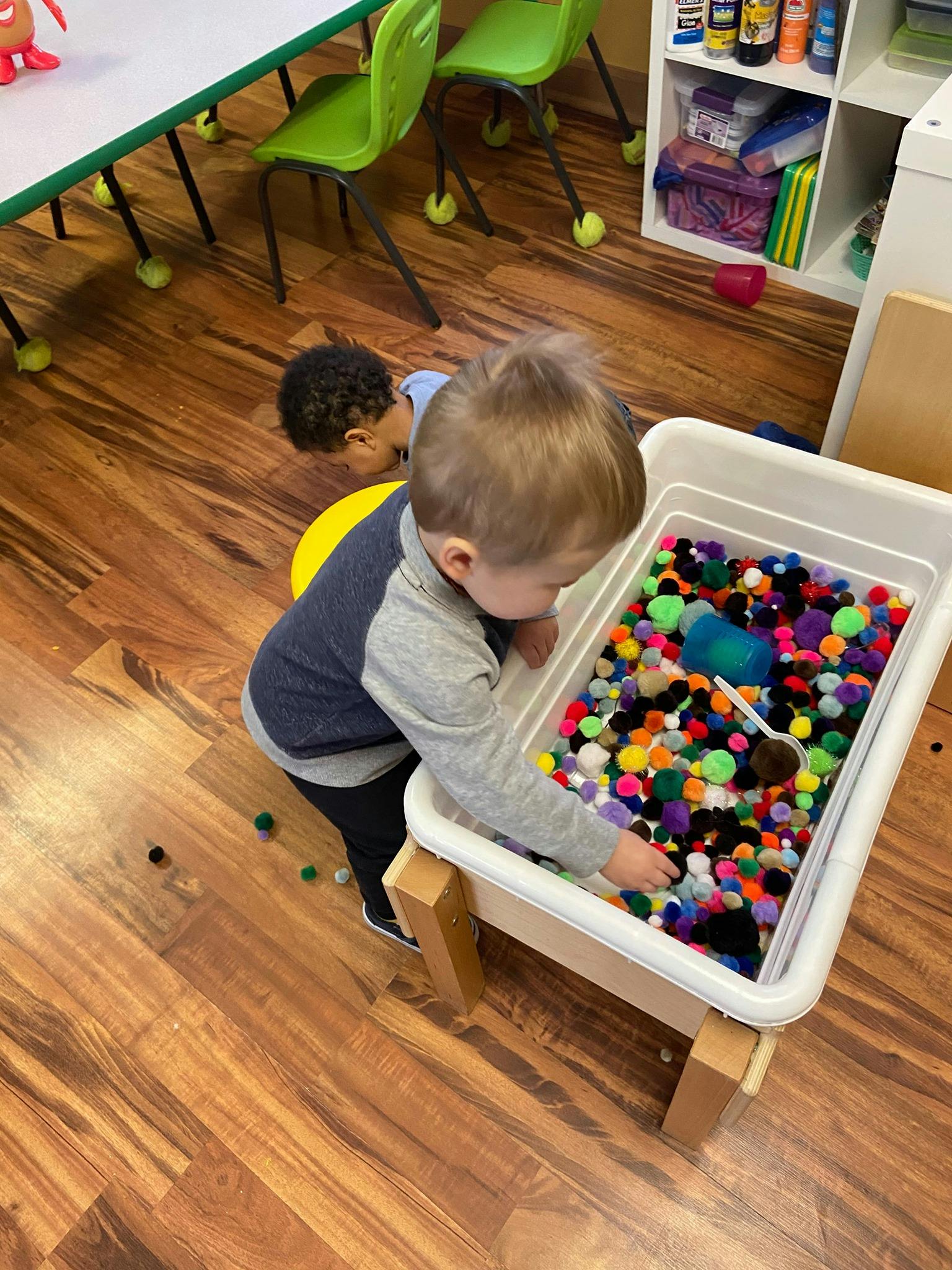 Child playing with colorful pom-poms in a sensory bin
