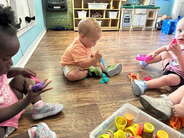 Three children playing with toys on a wooden floor