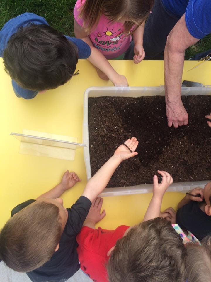 Children and an adult interacting with soil in a container