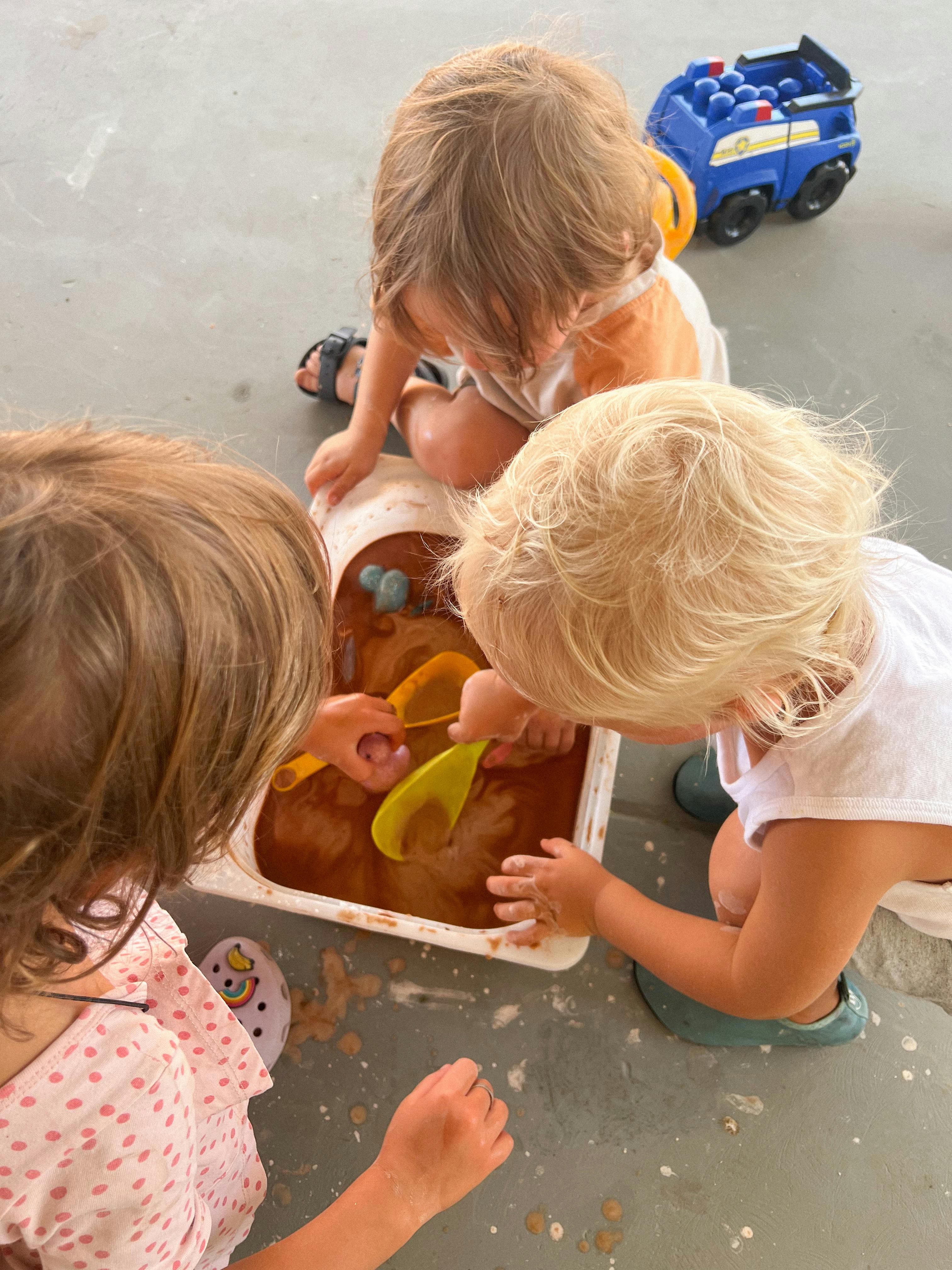 Three children playing with mud and toys in a container