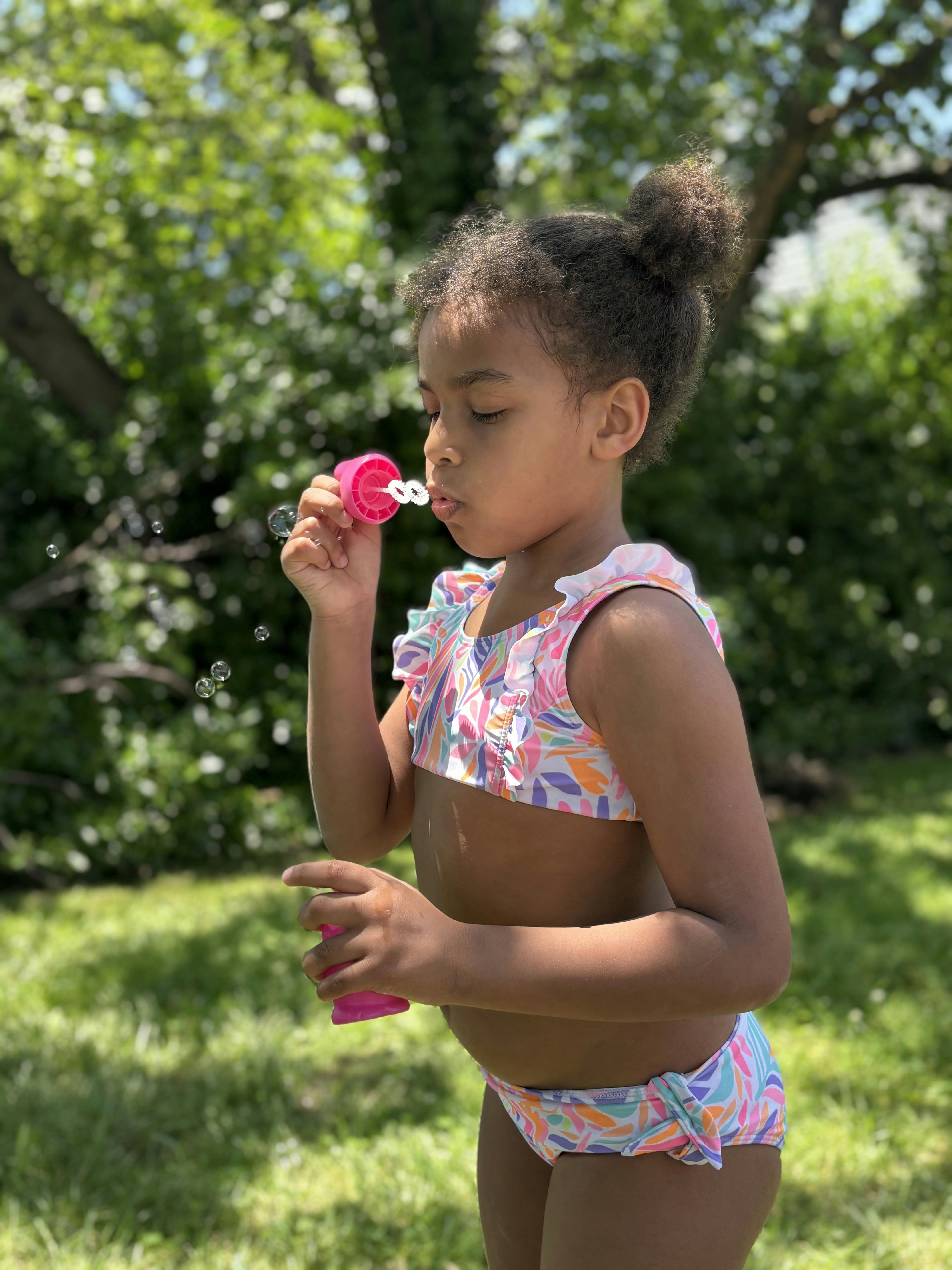 Child in a swimsuit blowing bubbles outdoors
