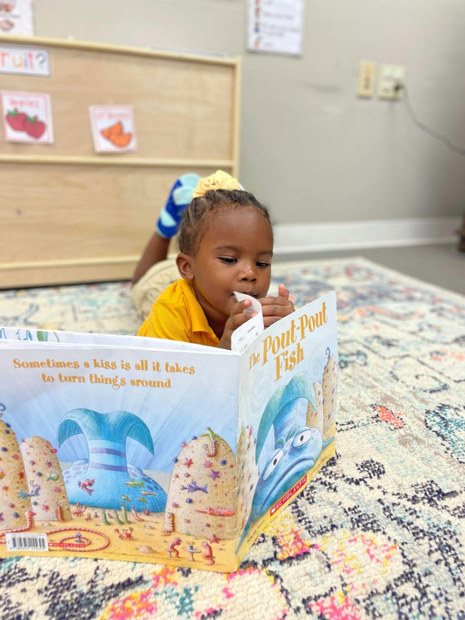 Child lying on a rug reading a book titled "The Pout-Pout Fish"