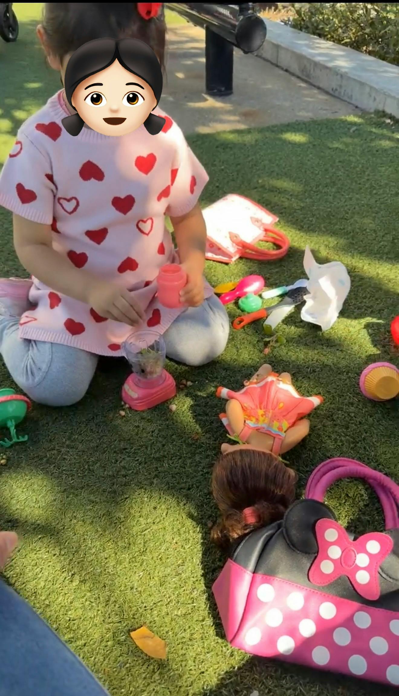 Child sitting on grass playing with a toy blender and other play accessories