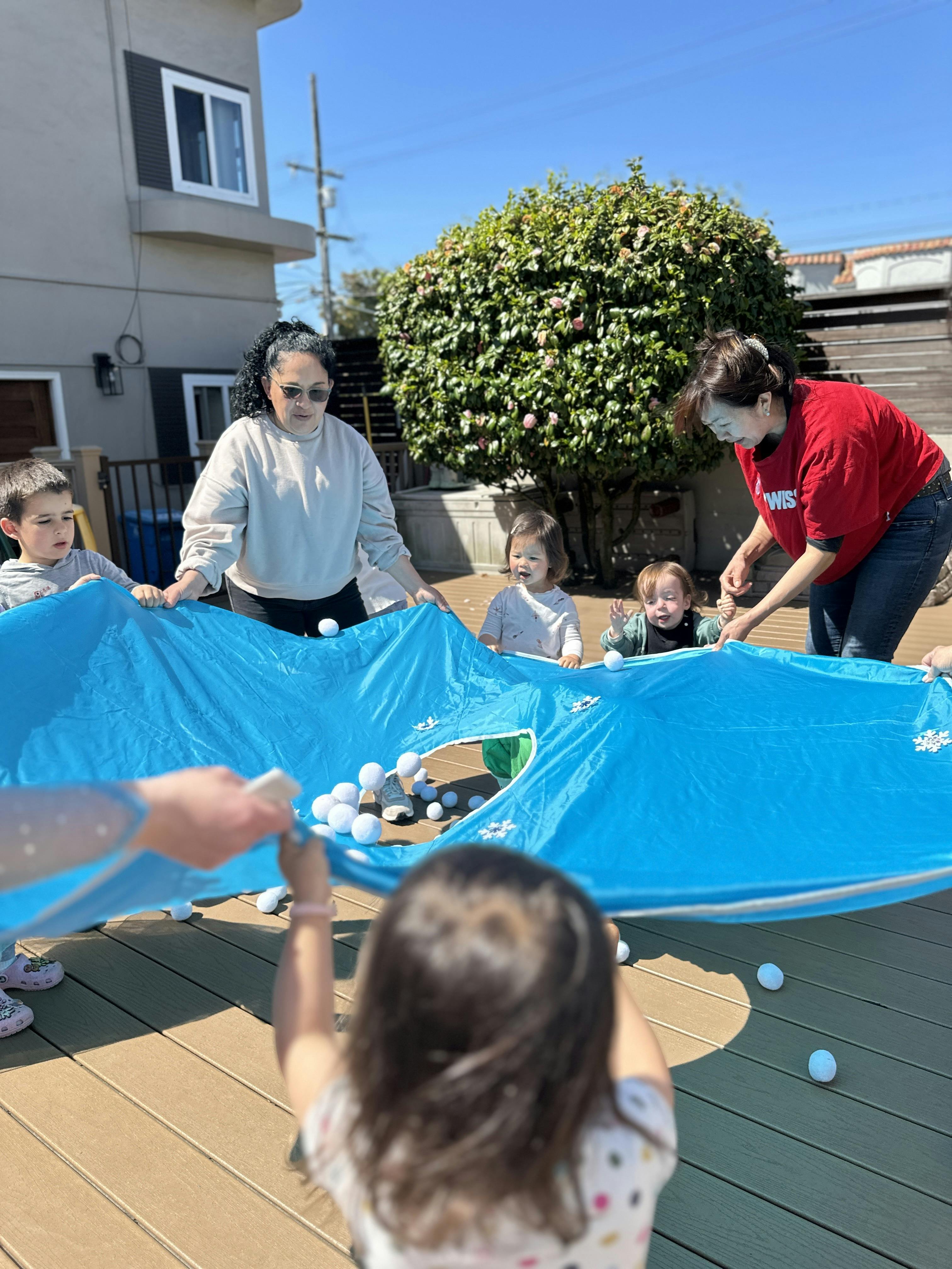 People holding a blue parachute game with white balls on an outdoor deck