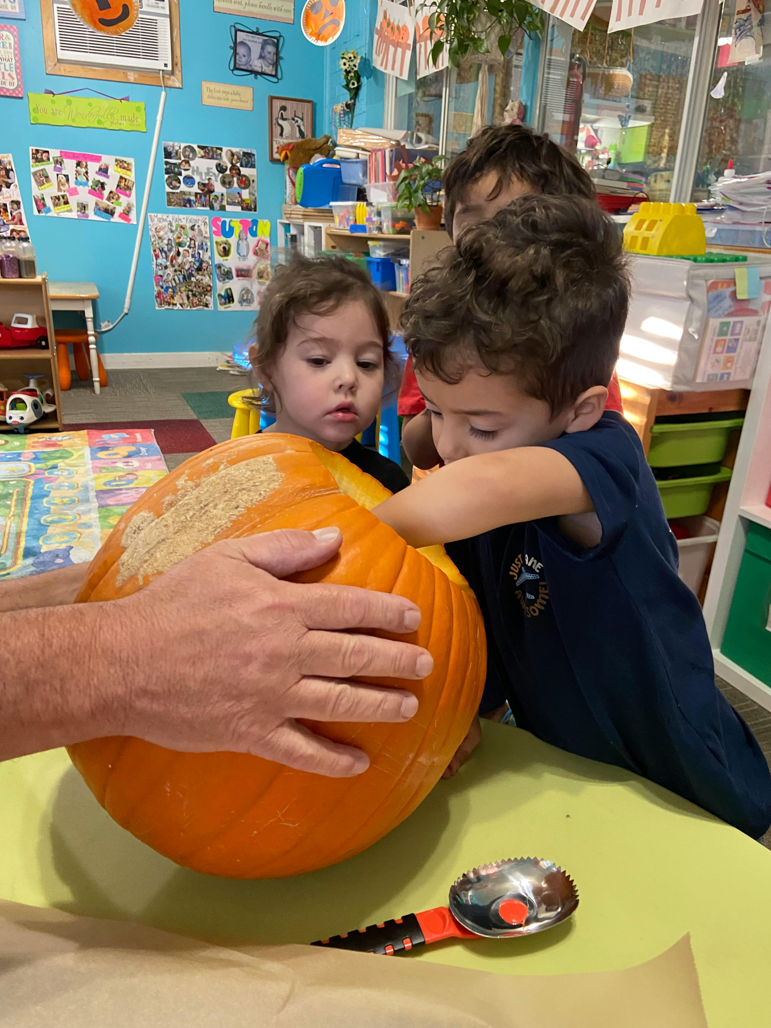 Adult and two children carving a pumpkin at a table