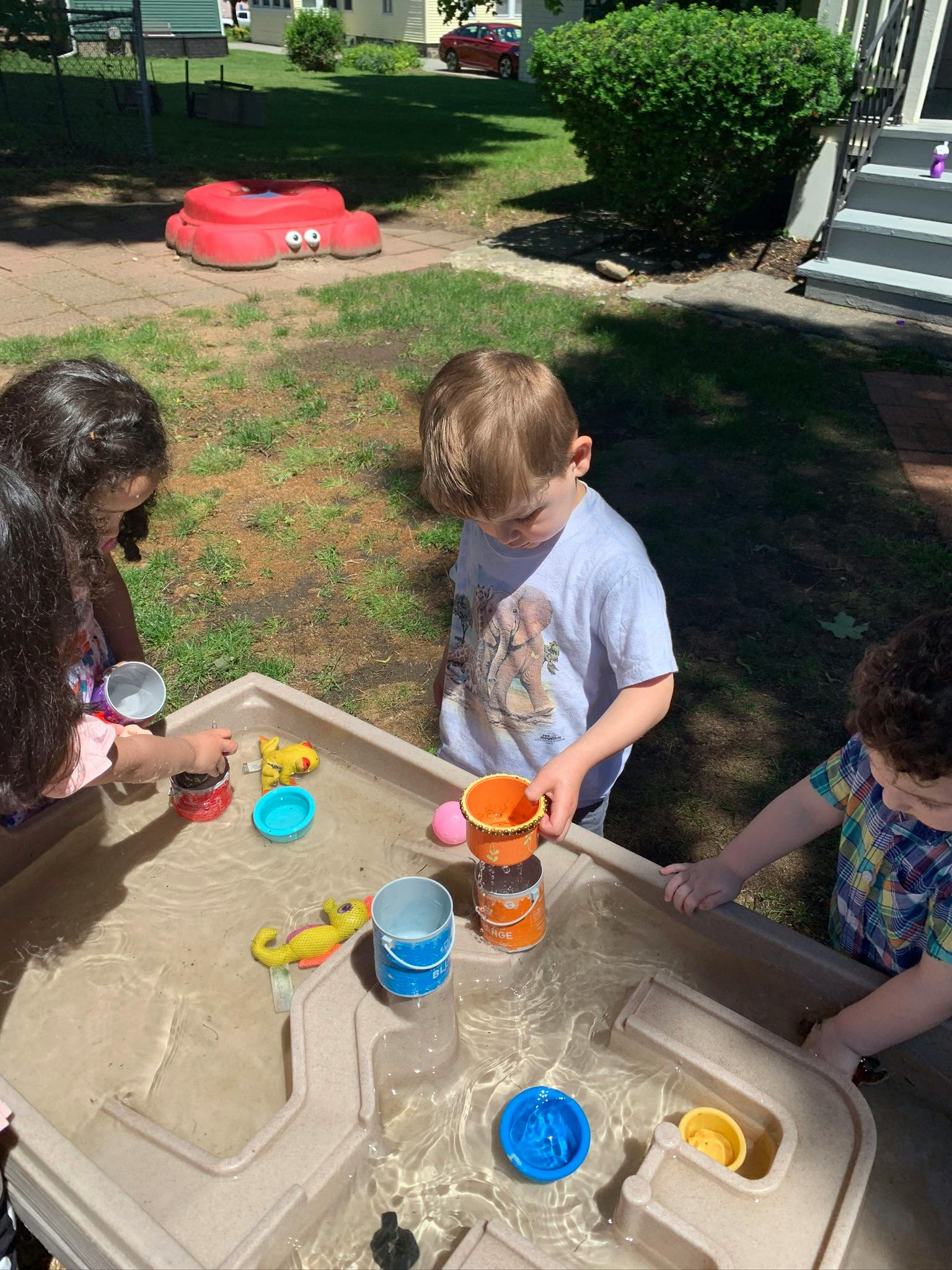 Three children playing with toys in a water table outdoors