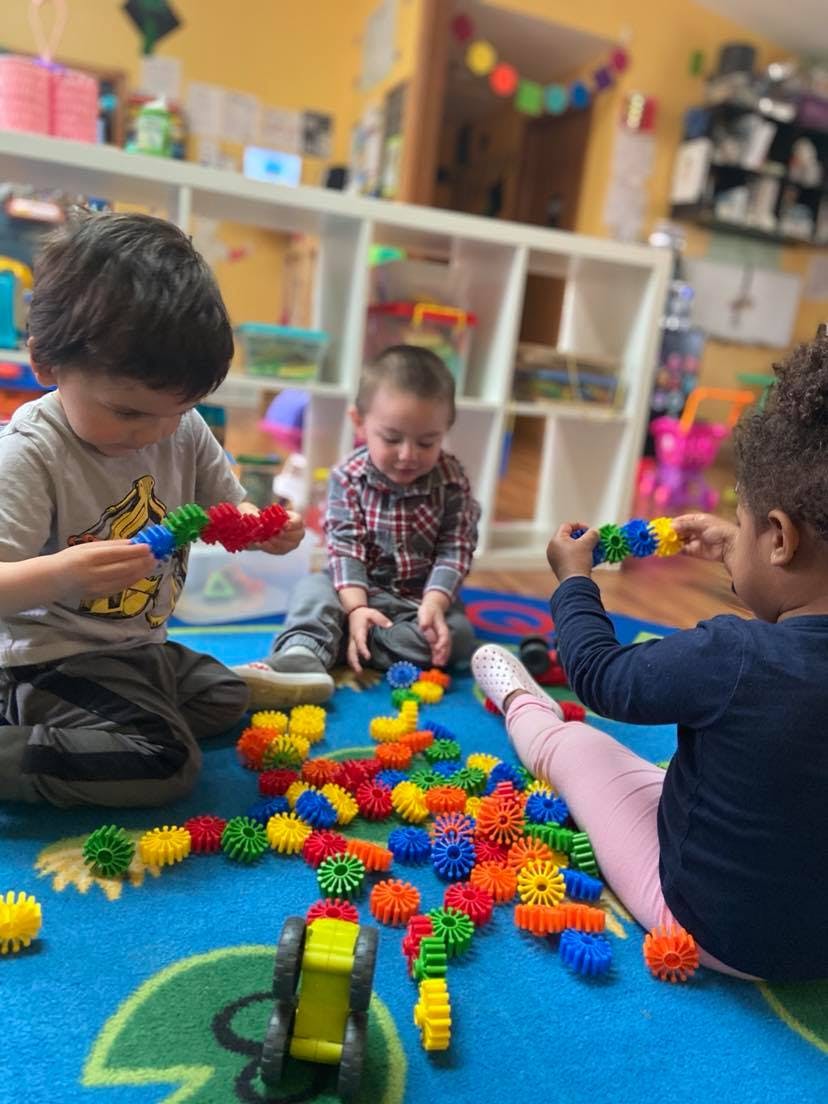 Three children playing with colorful interlocking toys on a blue rug