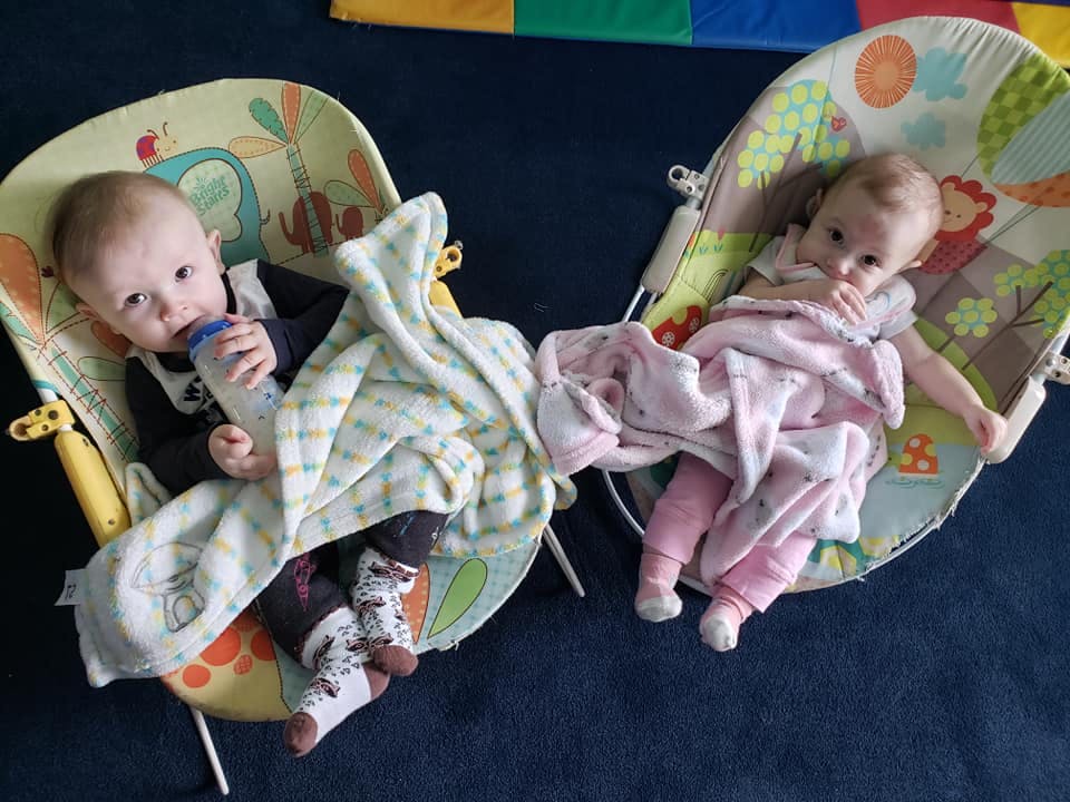 Two babies in bouncer seats, one drinking from a bottle