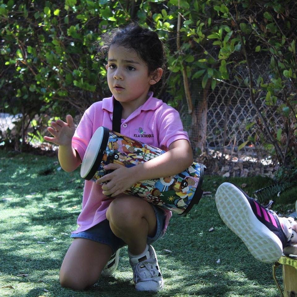 Child kneeling outdoors, holding a colorful drum
