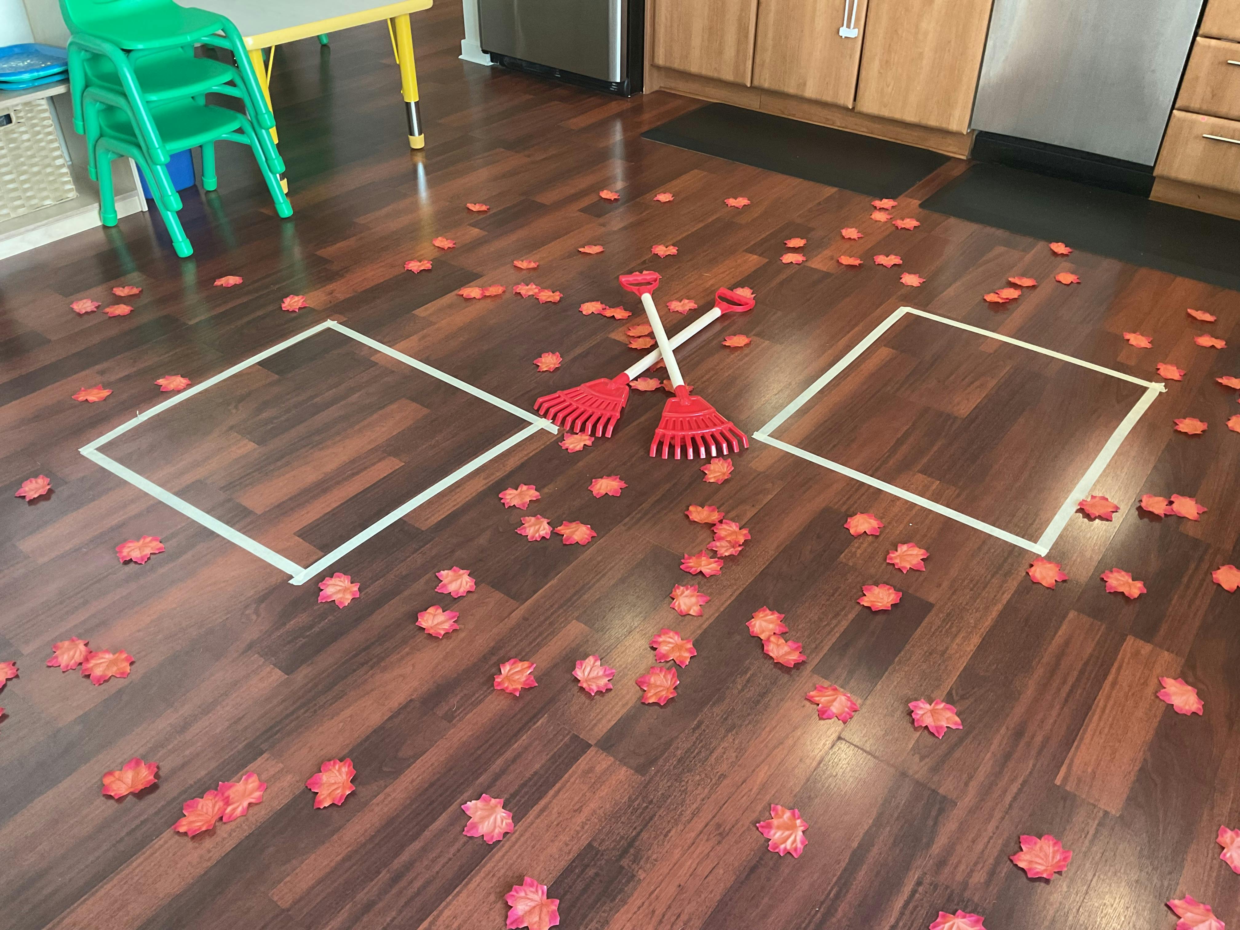 Red leaves scattered on a wooden floor with two small rakes