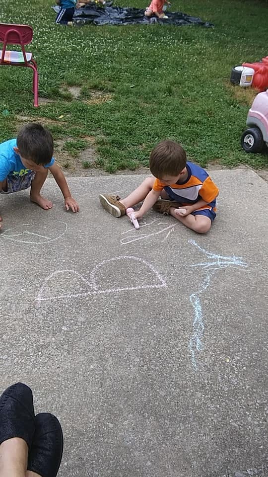 Two children drawing with chalk on a paved surface outdoors
