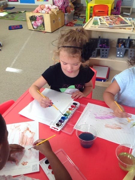 Child painting with watercolors at a red table in a classroom