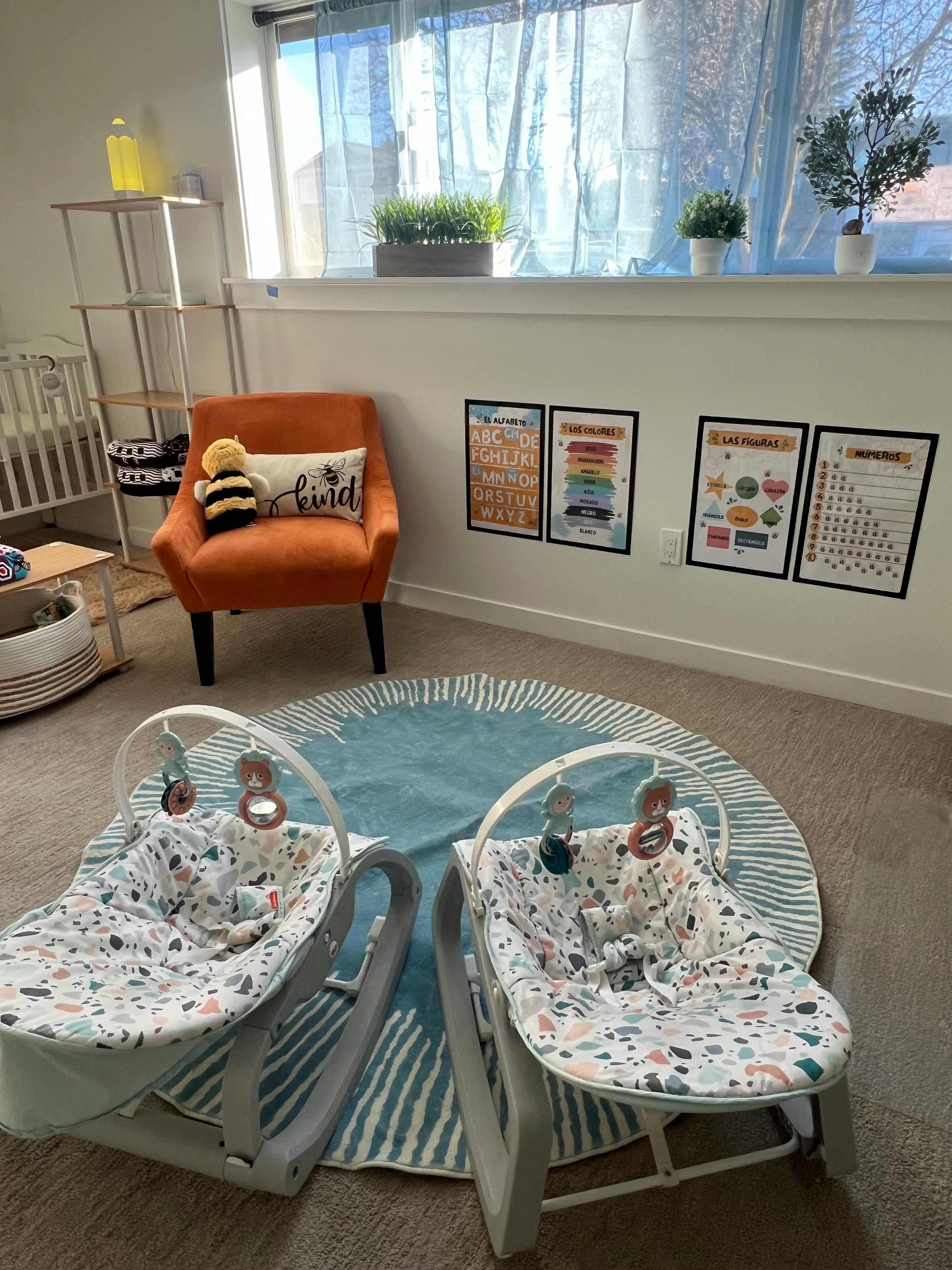Two baby bouncers on a blue rug in a room with an orange chair and posters