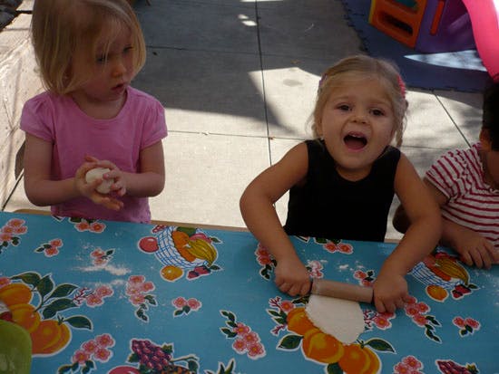 Child rolling dough with a rolling pin, another child holding dough