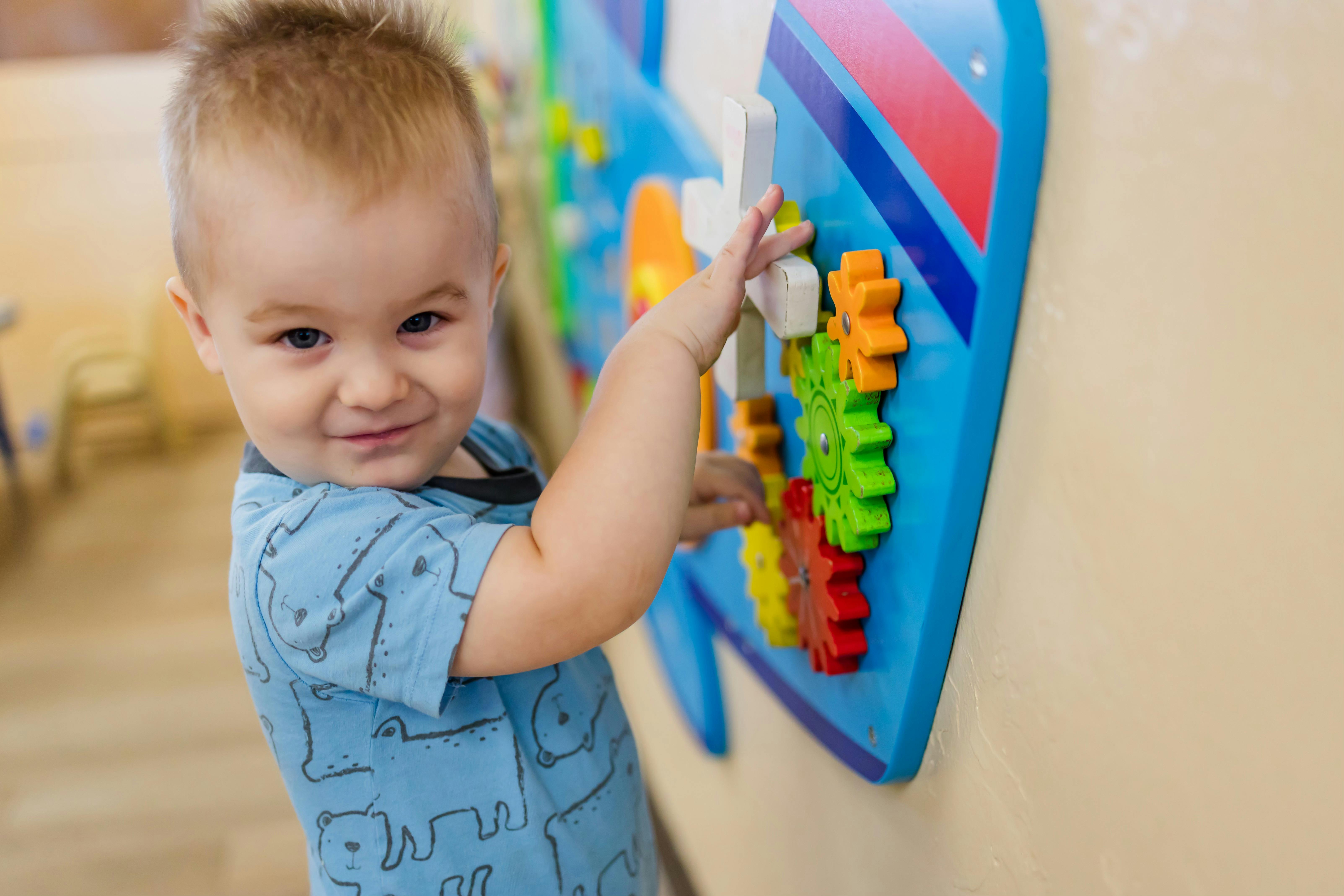 Child playing with a colorful gear toy on a wall
