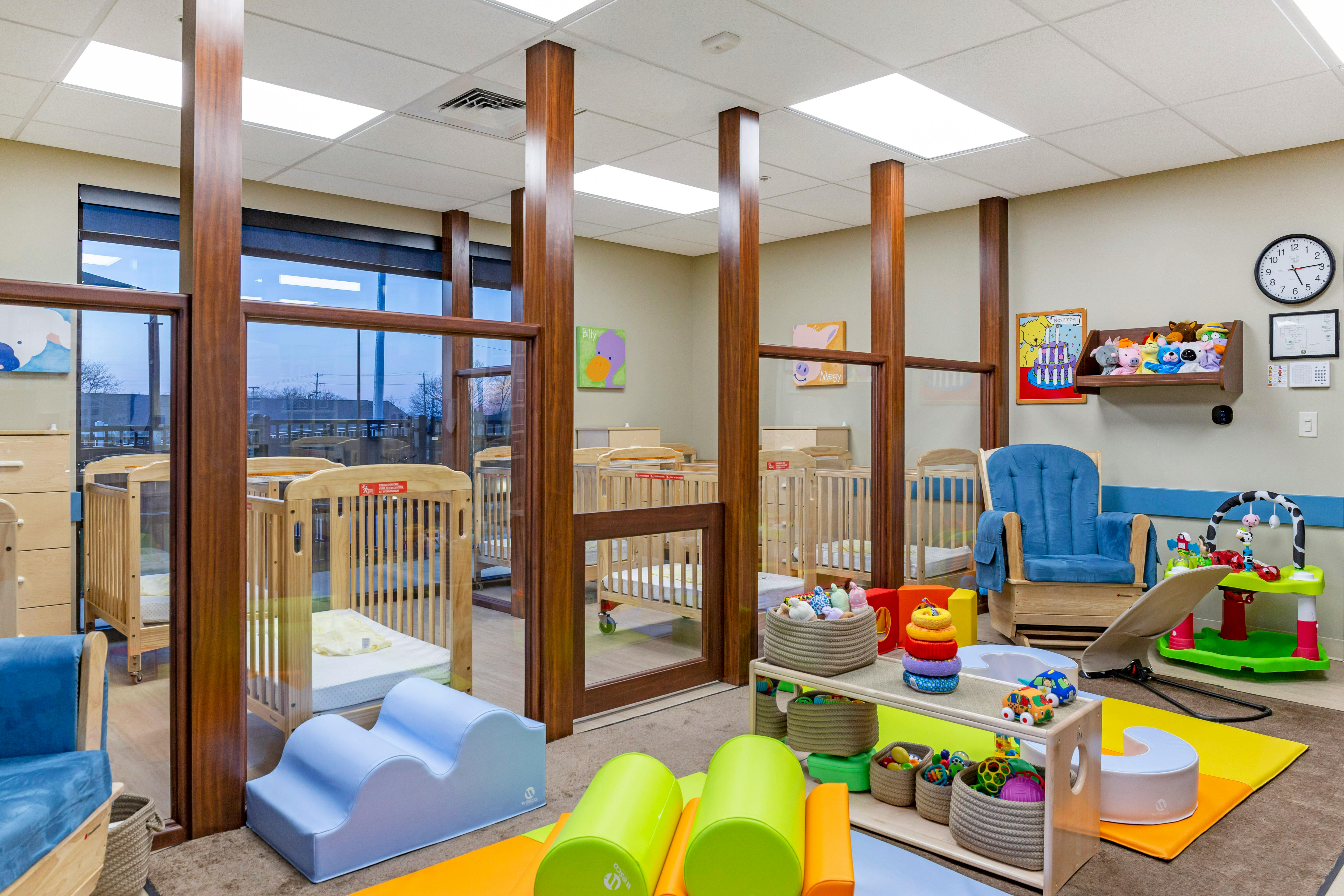 Baby room with multiple cribs separated by wooden dividers and glass panels