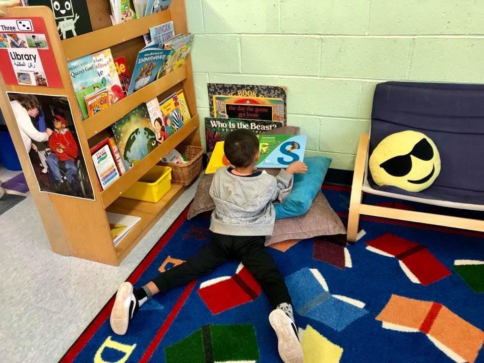 Child sitting on floor with pillows, holding a book with the letter S