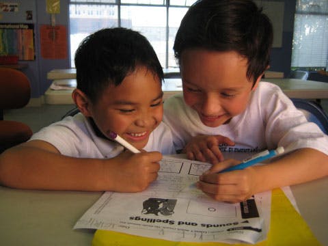 Two children writing on a paper with pens in a classroom