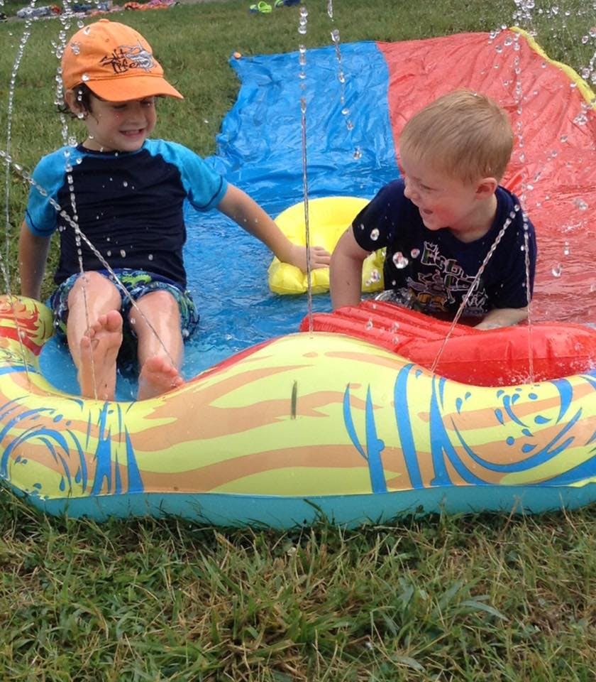 Two children playing on a water slide with water spraying