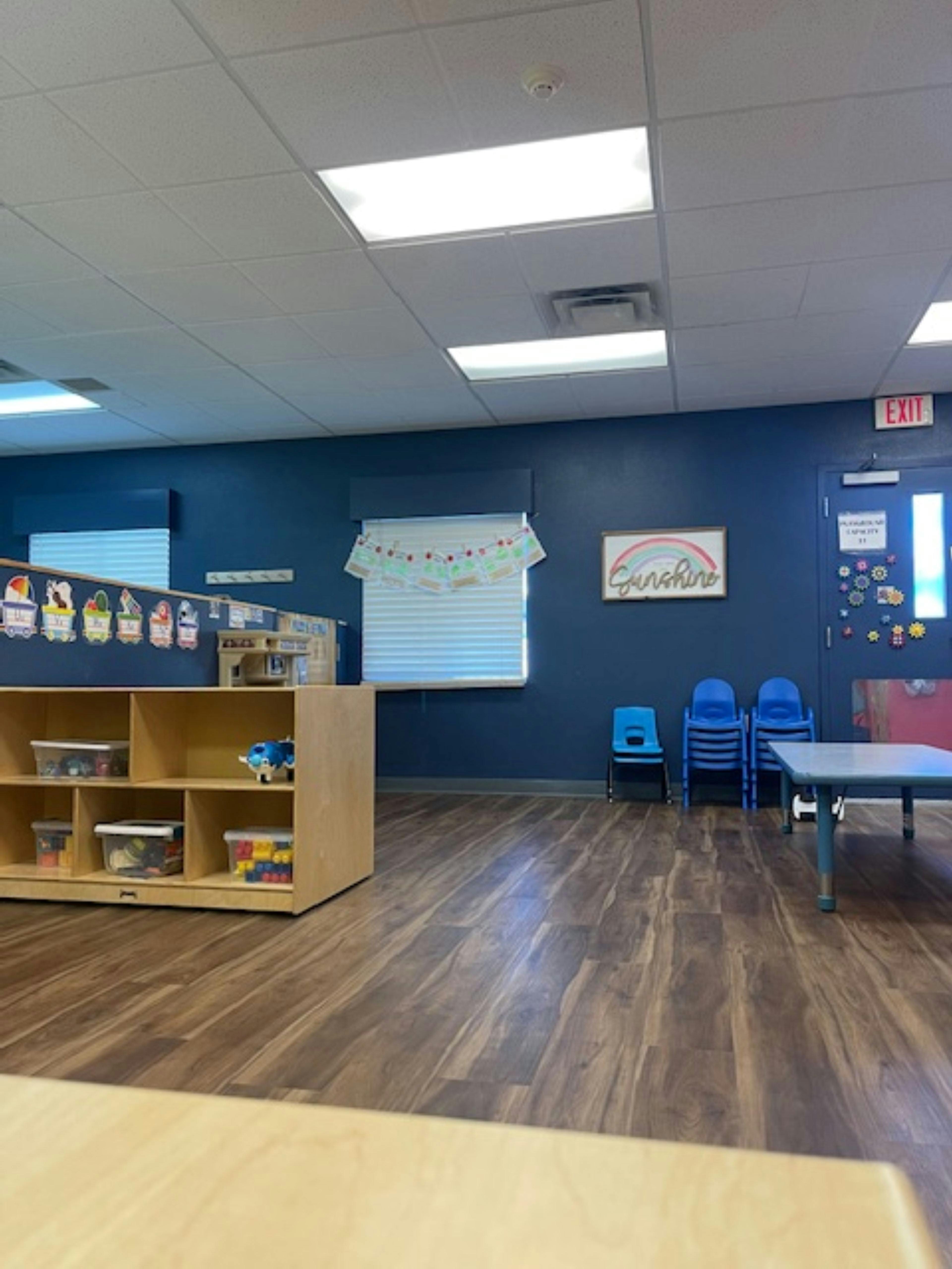 Empty classroom with blue walls, wooden floor, and child-sized furniture