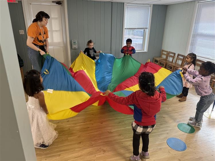 Adult and children playing with a colorful parachute indoors