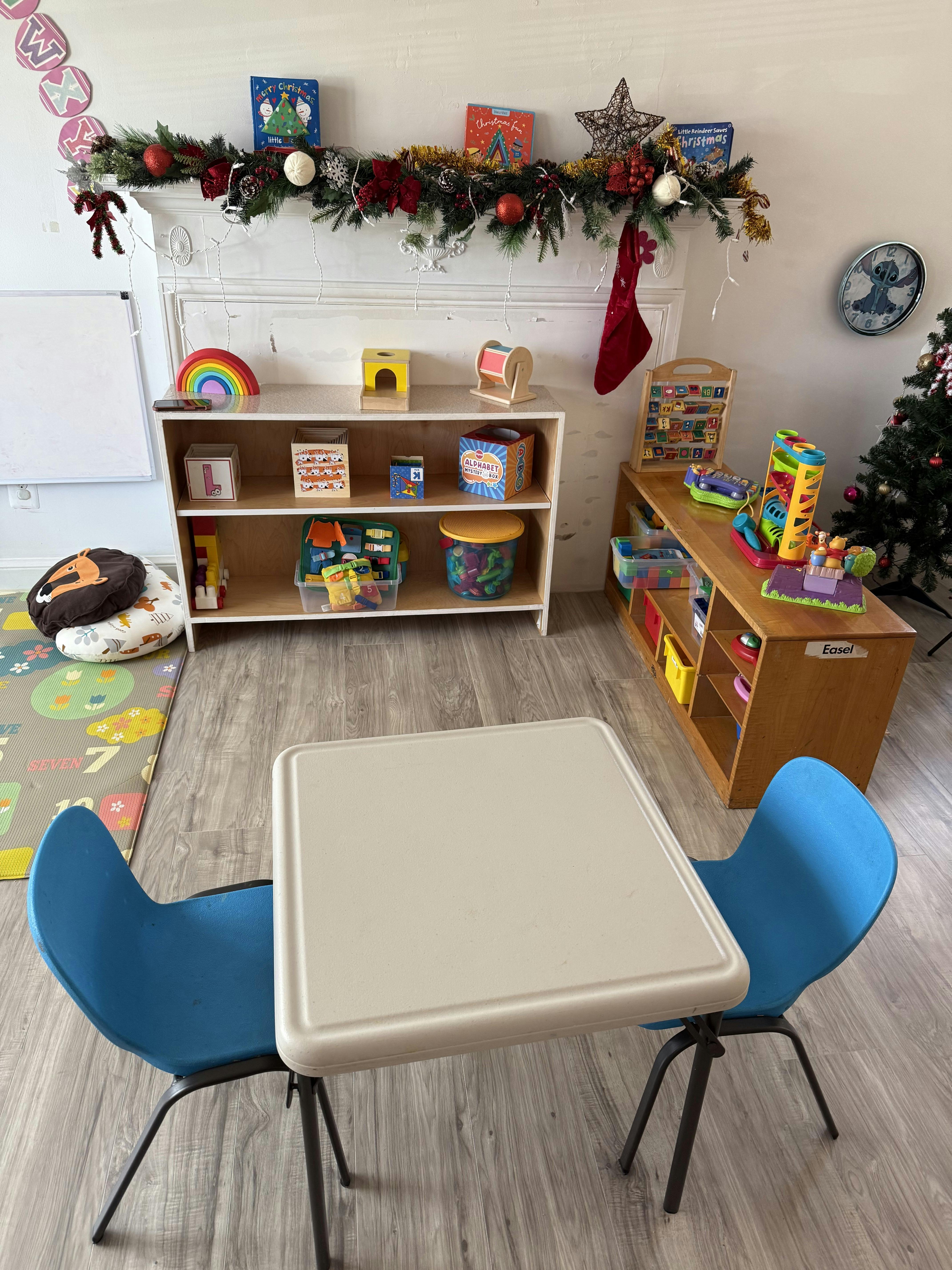 Classroom with shelves of toys and books, a small table, and two blue chairs