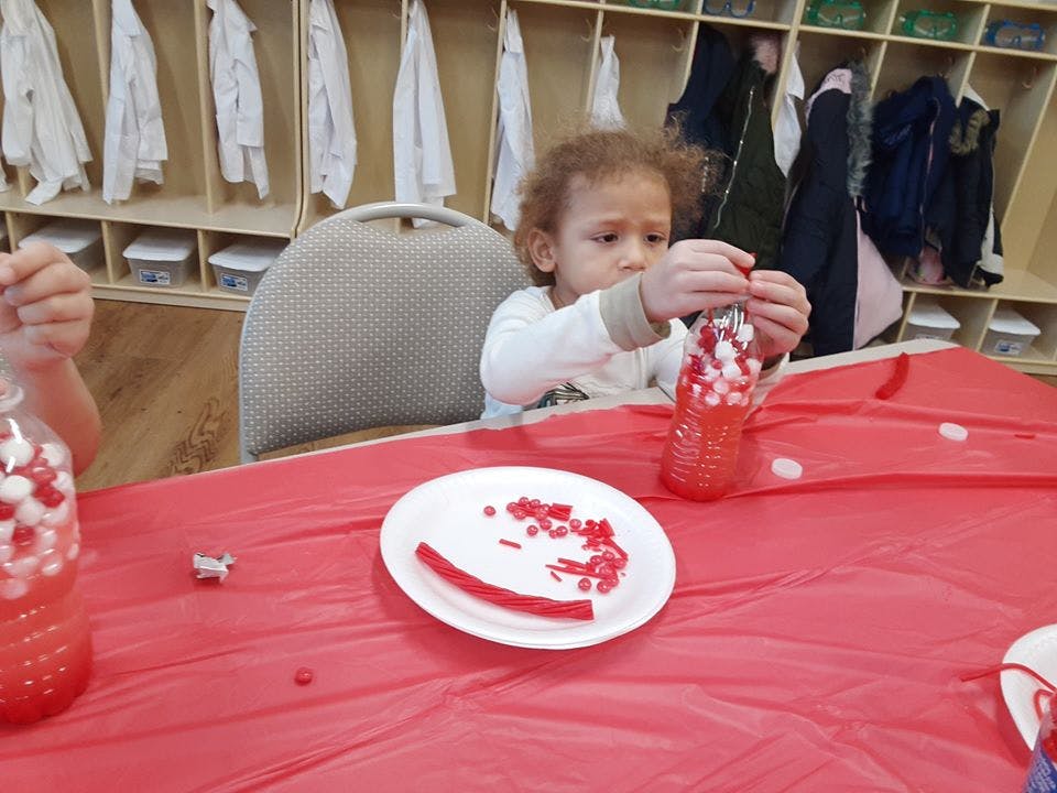 Child holding a bottle filled with small red and white objects