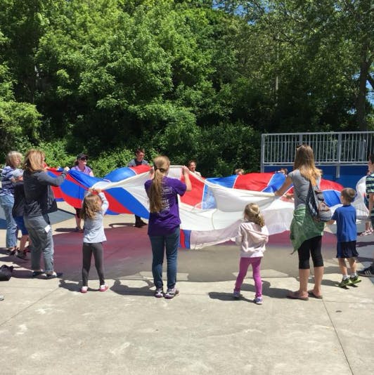 People and children holding a large red, white, and blue parachute