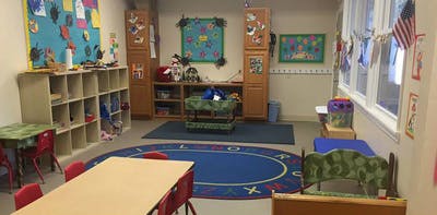 Classroom with tables, chairs, shelves, and a blue rug