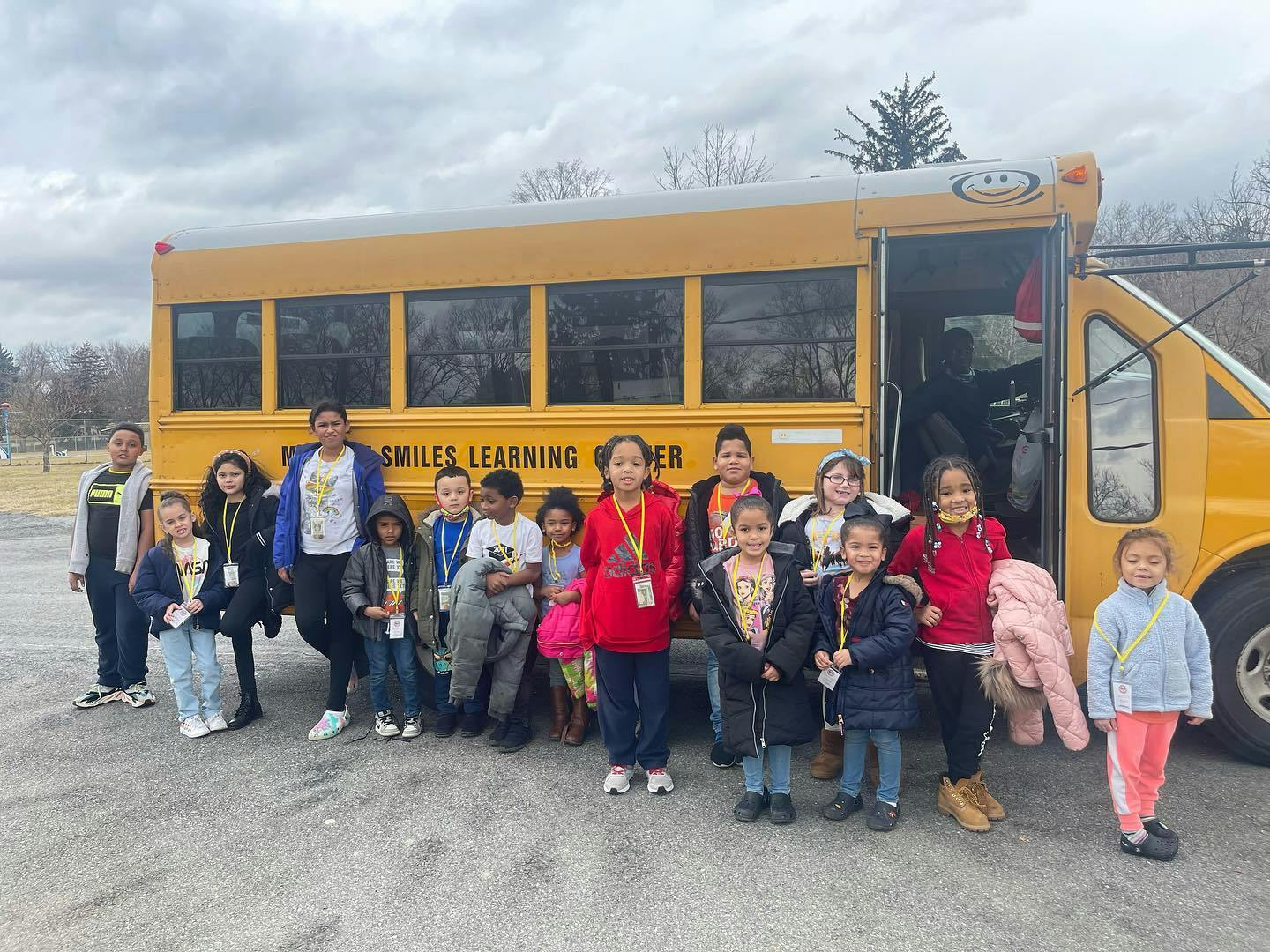 Group of children and adults standing in front of a yellow school bus