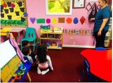 Adult standing in a classroom with two children on the floor