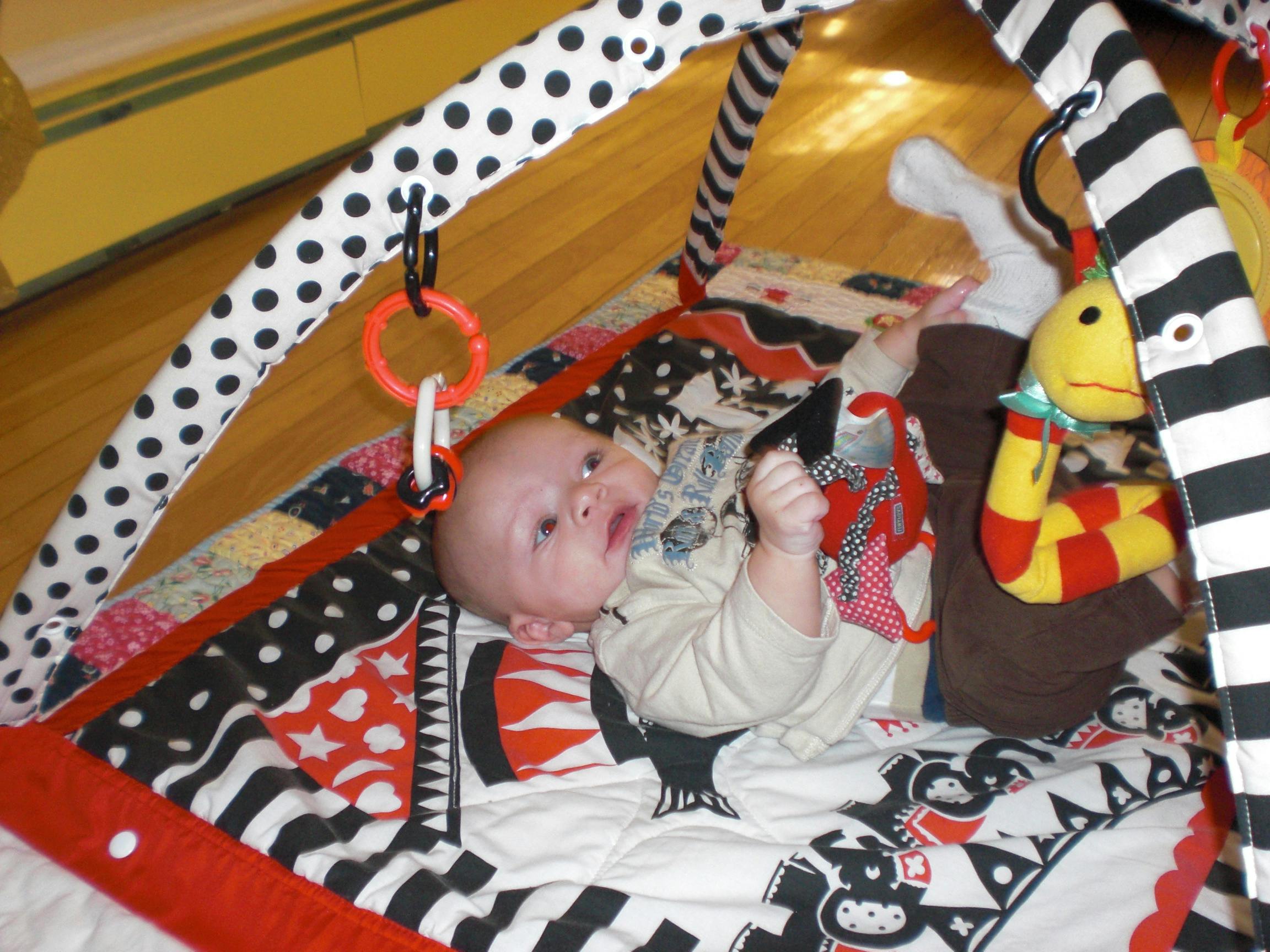 Child lying on a play mat under an activity arch