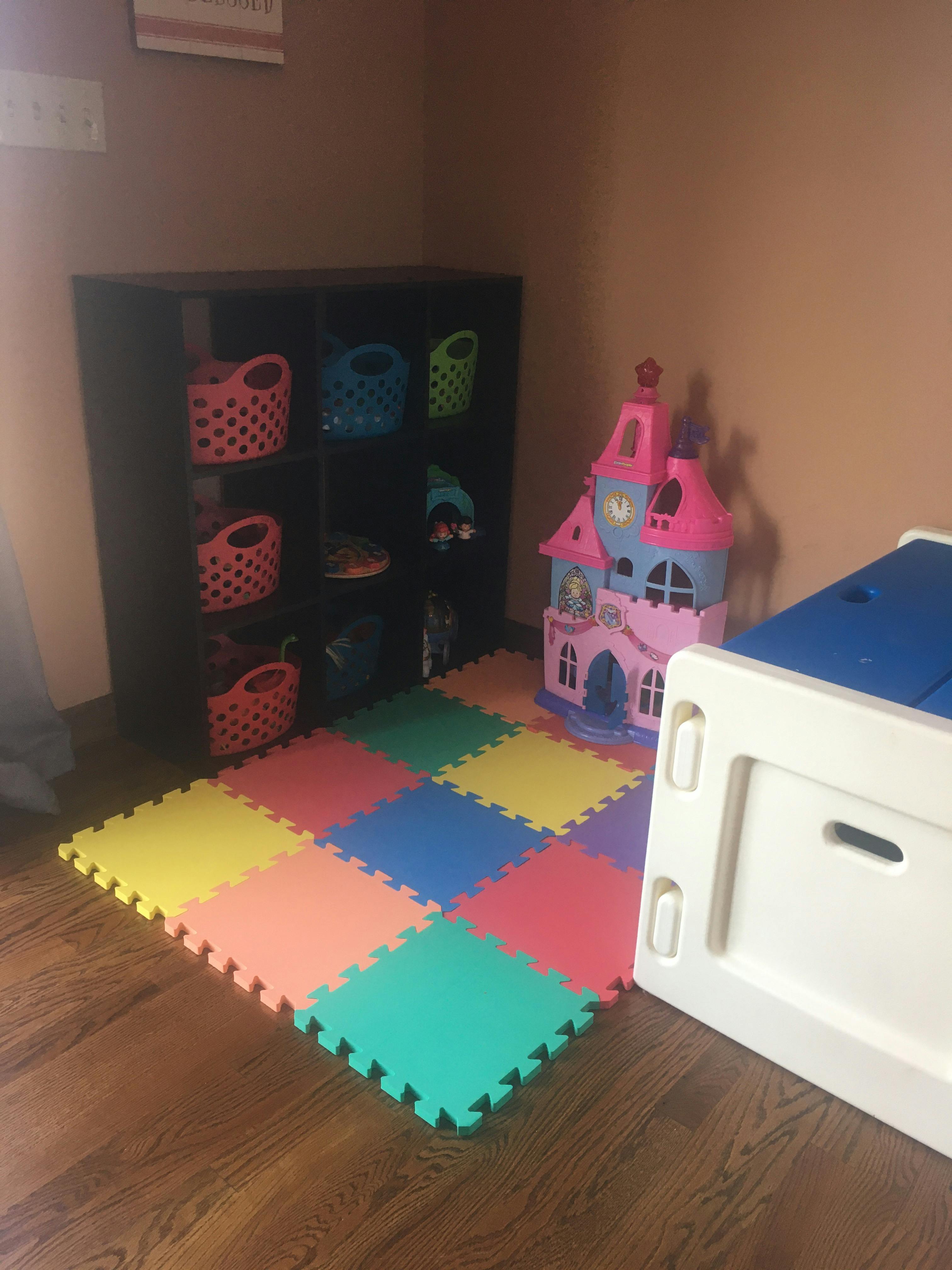 Colorful foam play mat on a wooden floor next to a toy castle and storage unit